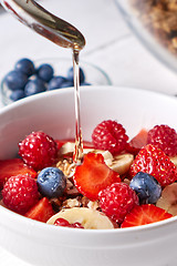 Image showing Healthy breakfast with fresh honey is pured into the flakes, muesli, raspberries, blueberries, strawberries on a gray wooden table. Close-up.