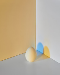 Image showing Painted egg on a gray-yellow double background with a reflection of blue-yellow shadows and copy space for text. Easter layout