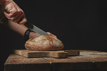 Image showing man slicing fresh organic bread on wooden board