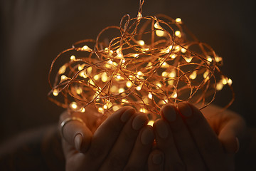 Image showing Woman hands holding string of lights in the dark.