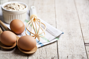 Image showing Fresh chicken eggs, oat flakes in ceramic bowl and kitchen utens