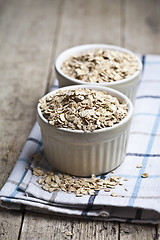 Image showing Raw oat flakes in ceramic bowls on linen napkin, golden wheat ea