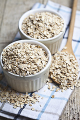 Image showing Oat flakes in ceramic bowls and wooden spoon on linen napkin, go