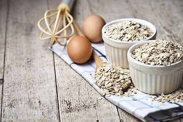 Image showing Fresh chicken eggs, oat flakes in ceramic bowls and wooden spoon