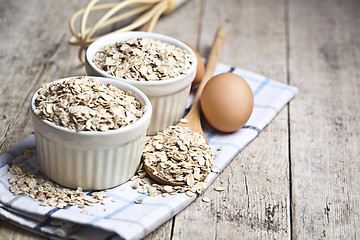 Image showing Oat flakes in ceramic bowls and wooden spoon and fresh chicken e