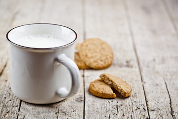 Image showing Cup of milk and some fresh baked oat cookies on rustic wooden ta