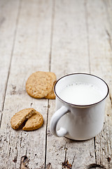 Image showing Cup of milk and some fresh baked oat cookies on rustic wooden ta