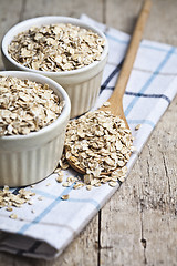 Image showing Oat flakes in ceramic bowls and wooden spoon on linen napkin, go