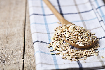 Image showing Oat flakes in wooden spoon on linen napkin, golden wheat ears on