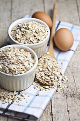 Image showing Oat flakes in ceramic bowls and wooden spoon and fresh chicken e