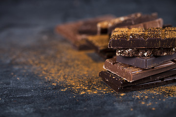 Image showing Broken chocolate stacked on black background. Chocolate bar piec