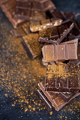 Image showing Broken chocolate stacked on black background. Chocolate bar piec