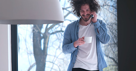 Image showing young man drinking coffee and using a mobile phone  at home