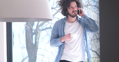 Image showing young man drinking coffee and using a mobile phone  at home