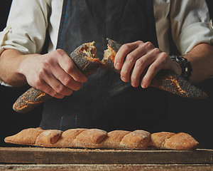 Image showing baker man holding fresh halves of a baguette