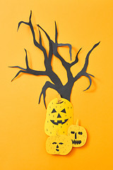 Image showing Handcraft paper tree and scary pumpkins on an orange background with space for text. Halloween layout. Flat lay