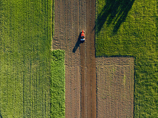 Image showing Aerial view from the drone, a bird\'s eye view of agricultural fields with a road through and a tractor on it in the spring evening at sunset in the summer