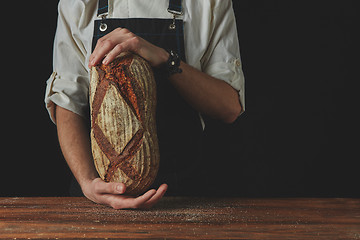 Image showing Baker\'s hands hold an oval bread.