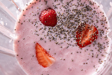 Image showing The process of preparing pink healthy cocktail with strawberries in a kitchen blender, close up. Top view