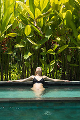 Image showing Sensual young woman relaxing in outdoor spa infinity swimming pool surrounded with lush tropical greenery of Ubud, Bali.