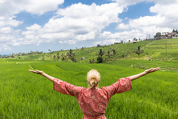 Image showing Relaxed fashionable caucasian woman wearing red asian style kimono, arms rised to sky, enjoying pure nature at beautiful green rice fields on Bali island