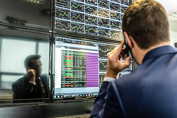 Image showing Stock broker trading online, talking on mobile phone.