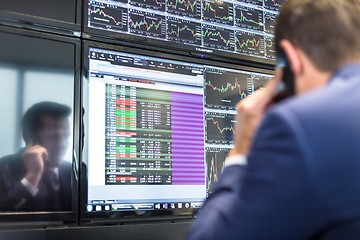 Image showing Stock broker trading online, talking on mobile phone.