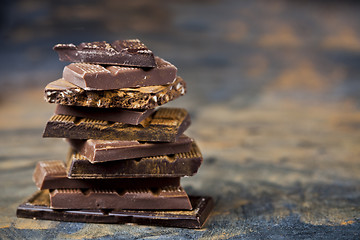 Image showing Broken chocolate stacked on black background. Chocolate bar piec