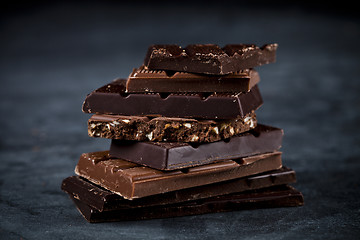Image showing Chocolate bars pieces stack on black background. Sweet food phot