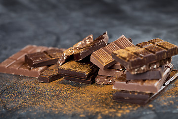 Image showing Broken chocolate stacked on black background. Chocolate bar piec