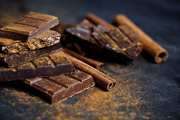 Image showing Chocolate bars pieces heap witn cinnamon powder and sticks. 