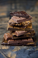 Image showing Broken chocolate stacked on black background. Chocolate bar piec