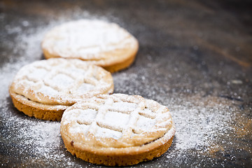 Image showing Fresh baked tarts with chocolate filling and sugar powder on bla