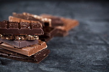 Image showing Chunks of broken chocolate stacked on black board. Chocolate bar