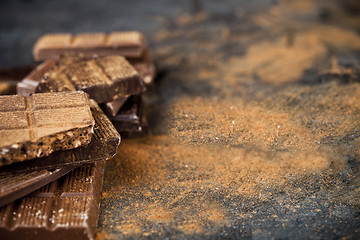 Image showing Broken chocolate  witn cinnamon powder stacked on black backgrou