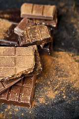 Image showing Broken chocolate stacked on black background. Chocolate bar piec