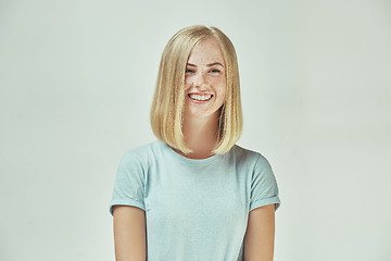 Image showing The happy freckled woman standing and smiling against gray background.