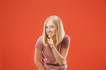 Image showing The young woman whispering a secret behind her hand over red background