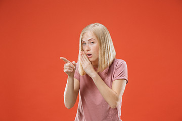 Image showing The young woman whispering a secret behind her hand over red background