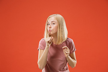 Image showing The young woman whispering a secret behind her hand over red background