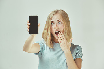 Image showing Portrait of a confident casual girl showing blank screen mobile phone isolated over gray background