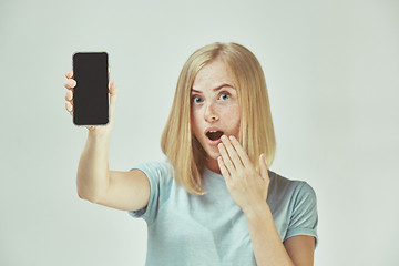 Image showing Portrait of a confident casual girl showing blank screen mobile phone isolated over gray background