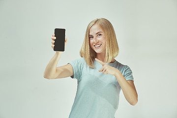 Image showing Portrait of a confident casual girl showing blank screen mobile phone isolated over gray background