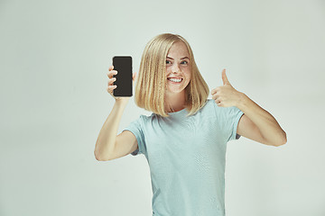 Image showing Portrait of a confident casual girl showing blank screen mobile phone isolated over gray background