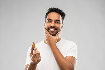 Image showing smiling indian man applying grooming oil to beard