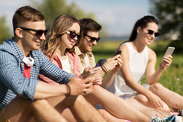 Image showing smiling friends with smartphones sitting on grass