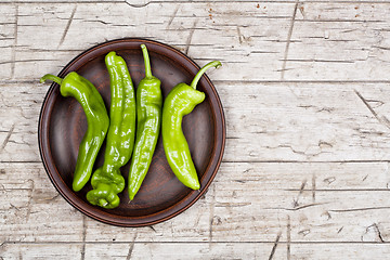 Image showing Fresh green raw peppers on brown ceramic plate on rustic wooden 