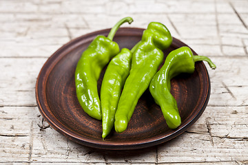 Image showing Fresh green raw peppers on brown ceramic plate on rustic wooden 
