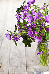 Image showing Wild violet flowers in glass bottle on rustic wooden table backg