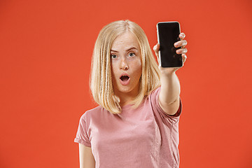 Image showing Portrait of a confident casual girl showing blank screen mobile phone isolated over red background